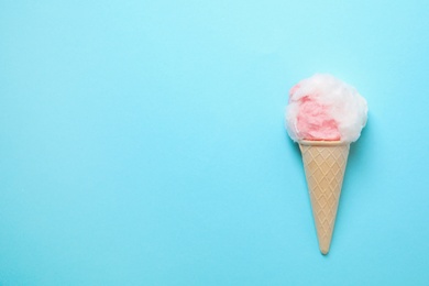 Ice cream cone with fluffy cotton candy and space for text on color background, top view