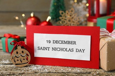 Card with text 19 December Saint Nicholas Day and festive decor on wooden table, closeup