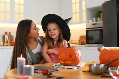 Mother and daughter with pumpkin jack o'lantern at table in kitchen. Halloween celebration