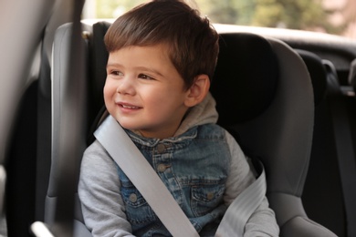 Cute little child sitting in safety seat inside car. Danger prevention
