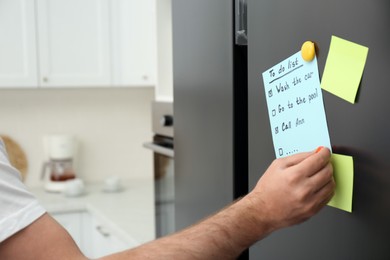 Man putting to do list on refrigerator door in kitchen, closeup