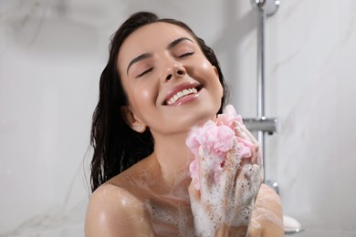 Young woman with mesh pouf taking shower at home