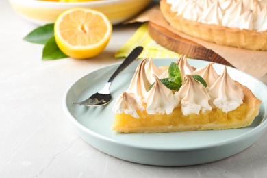 Piece of delicious lemon meringue pie with mint served on light table, closeup