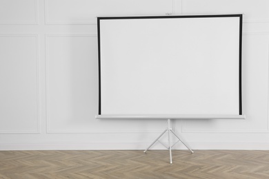 Blank projection screen near white wall indoors. Space for design
