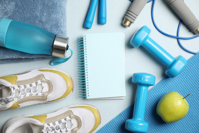 Flat lay composition with fitness equipment and notebook on light blue background, space for text