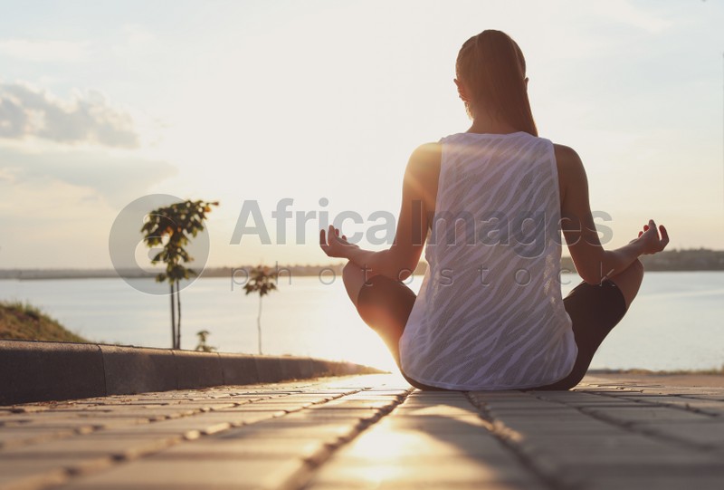 Young woman meditating near river in morning, back view. Space for text