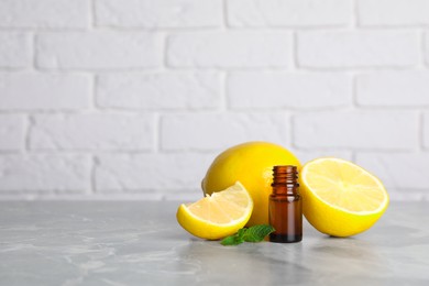 Bottle of essential oil with lemons and mint on grey marble table against white brick wall. Space for text