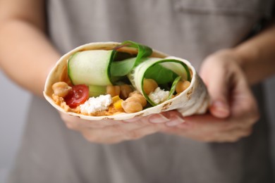 Woman holding delicious hummus wrap with vegetables, closeup