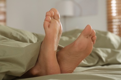 Person in bed with green linens at home, closeup on feet