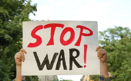 Photo of Woman holding poster with words Stop War outdoors, closeup