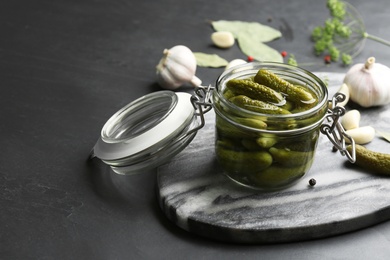 Glass jar of pickled cucumbers on black table. Space for text