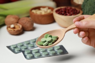 Woman holding spoon of pills at table with foodstuff, closeup. Prebiotic supplements