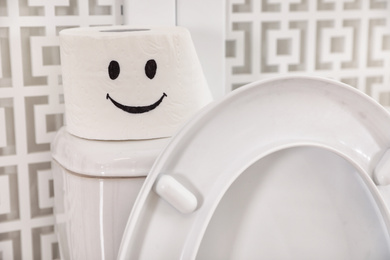 Roll of paper with funny face on toilet tank in bathroom, closeup
