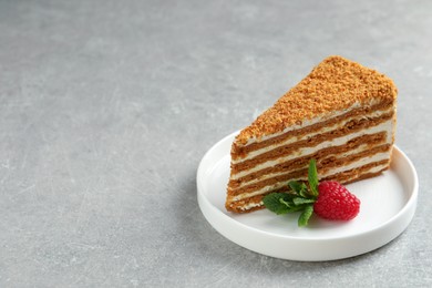 Slice of delicious layered honey cake with mint and raspberry on grey table. Space for text