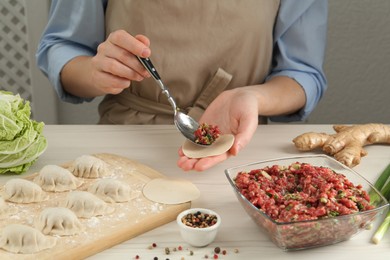 Woman putting gyoza filling in center of dough wrapper at white wooden table, closeup