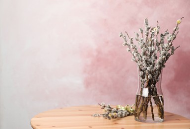 Beautiful pussy willow branches on wooden table against pink background, space for text