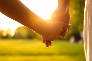 Little girl and her mother holding hands in park, closeup. Happy family