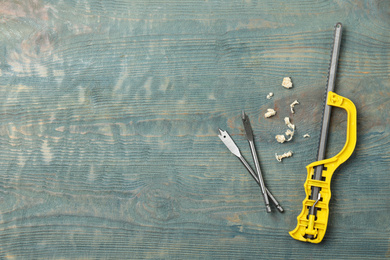 Small hand saw, spade drill bits and shavings on blue wooden background, flat lay with space for text. Carpenter's tools