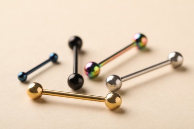 Different stylish barbells on beige background, closeup. Piercing jewelry