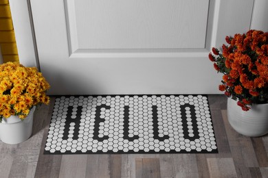 Stylish door mat with word Hello and beautiful flowers on wooden floor