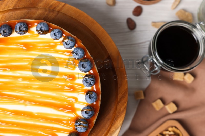 Delicious cheesecake with caramel and blueberries on white wooden table, top view. Space for text