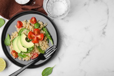 Photo of Delicious quinoa salad with tomatoes, avocado slices and spinach leaves served on white marble table, flat lay. Space for text