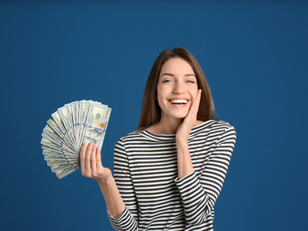 Happy young woman with cash money on blue background