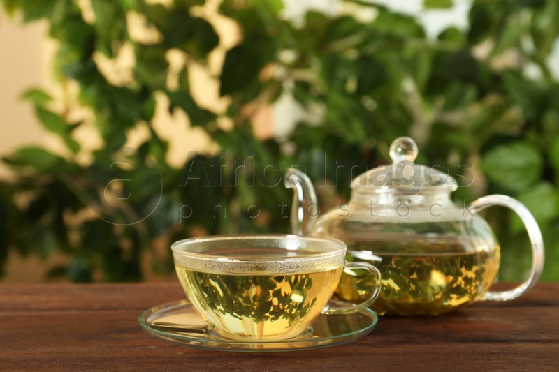 Photo of Fresh green tea in glass cup and teapot on wooden table