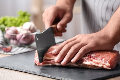 Man cutting fresh raw meat on table in kitchen, closeup