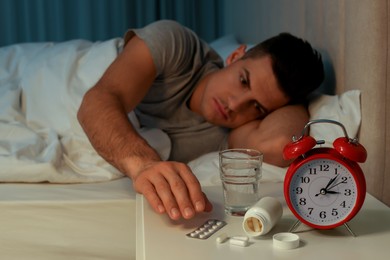 Man suffering from insomnia in bed at home, focus on pills and alarm clock