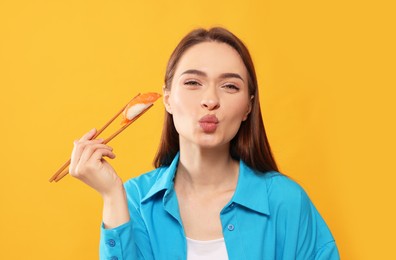 Photo of Funny young woman holding sushi with chopsticks on orange background