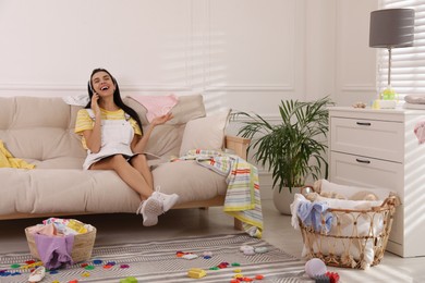 Young mother with magazine talking by mobile phone on sofa in messy living room
