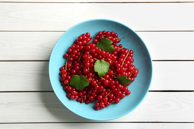 Delicious red currants and leaves on white wooden table, top view