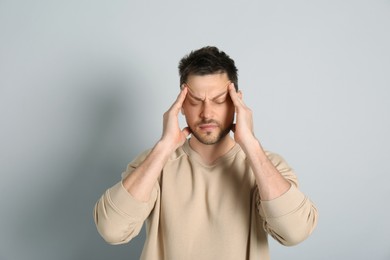Man suffering from terrible migraine on light grey background