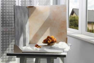 Stand with juicy peaches and double-sided backdrops on table in photo studio