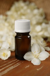 Bottle of jasmine essential oil and white flowers on wooden table, closeup