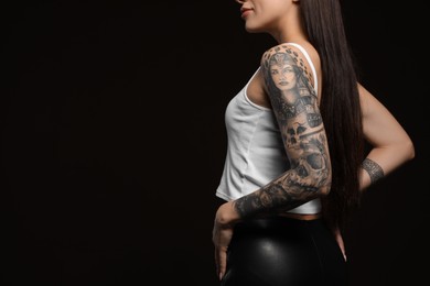 Beautiful woman with tattoos on arms against black background, closeup. Space for text
