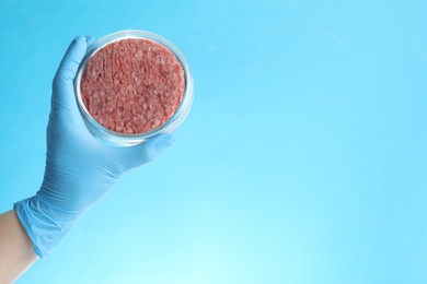 Photo of Scientist holding Petri dish with minced lab grown meat on light blue background, closeup. Space for text