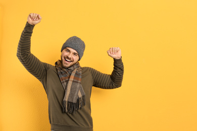 Happy young man in warm clothes on yellow background, space for text. Winter vacation