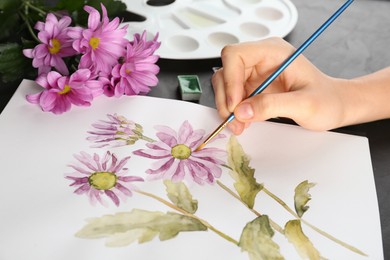 Woman drawing beautiful chrysanthemum flowers in sketchbook at black table, closeup