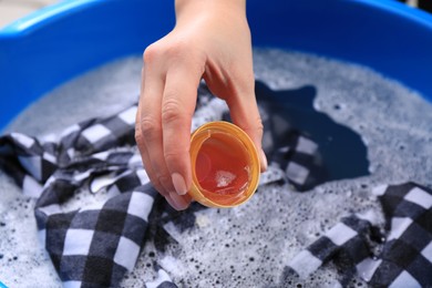 Woman pouring detergent into basin with clothing, closeup. Hand washing laundry
