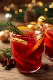 Delicious punch drink with cranberries and orange on wooden table against blurred festive lights, closeup