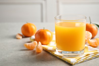 Photo of Glass of fresh tangerine juice and fruits on light grey table. Space for text