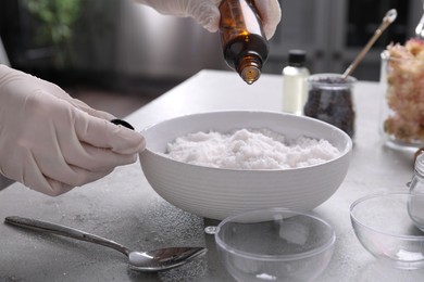 Woman in gloves adding essential oil to bath bomb mixture at grey table, closeup