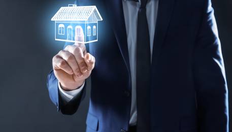 Real estate agent touching house illustration on virtual screen against dark background, closeup