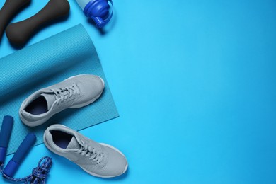 Exercise mat, shoes, dumbbells, shaker and skipping rope on turquoise background, flat lay. Space for text