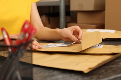 Post office worker sticking barcode on parcel at counter indoors, closeup
