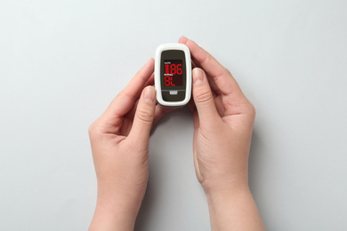 Photo of Woman holding fingertip pulse oximeter on white background, top view