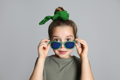Surprised little girl with stylish bandana and sunglasses on grey background