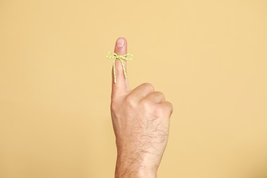 Man showing index finger with tied bow as reminder on beige background, closeup